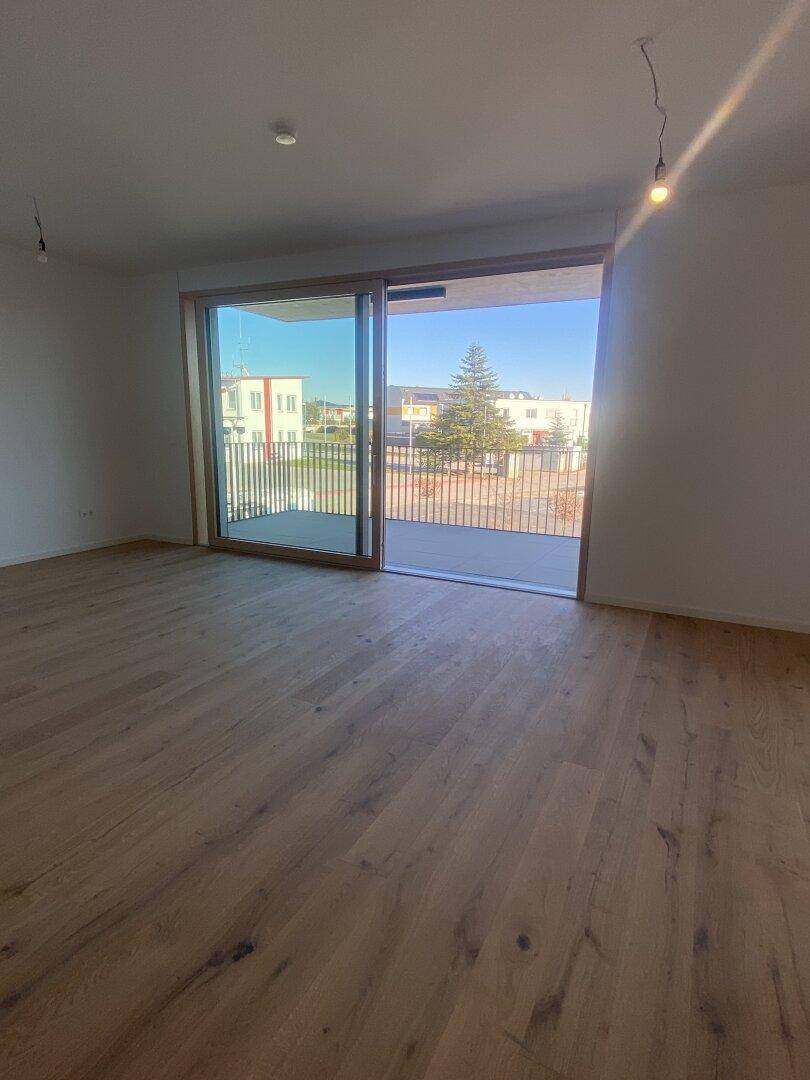 Geräumiges Wohnzimmer mit Holzboden und großer Schiebetür, die auf einen Balkon führt.