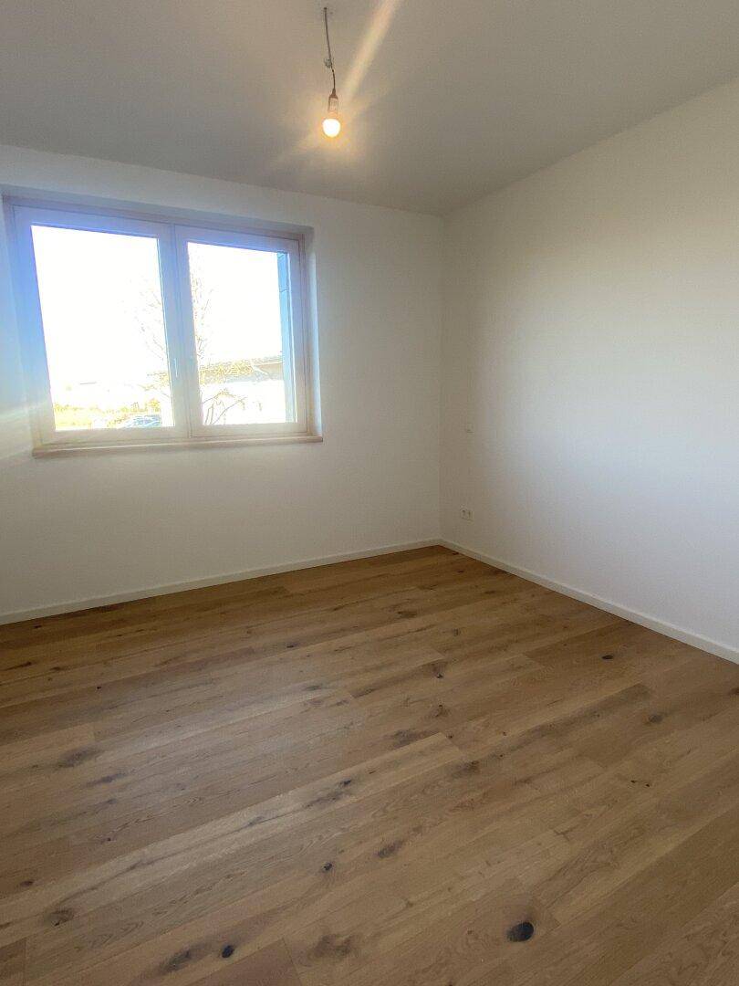 Leeres Zimmer mit hellem Holzboden und einem großen Fenster, das den Raum mit Licht füllt.