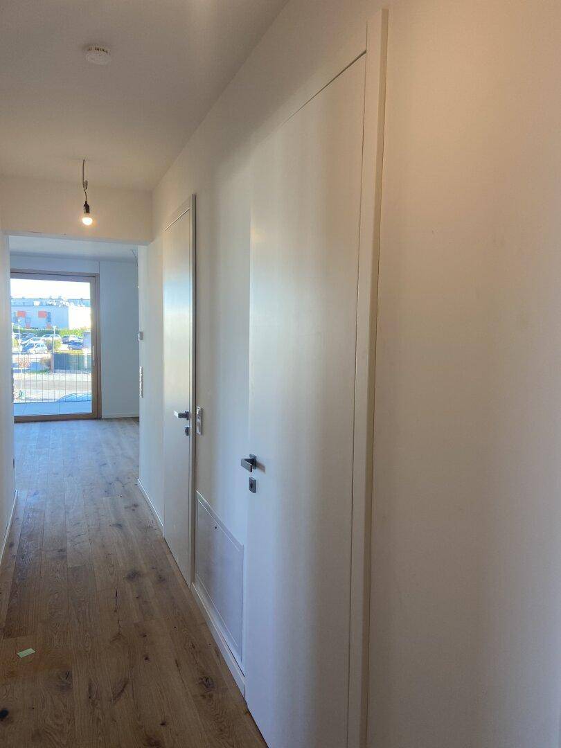 Heller Flur mit Holzboden, weißen Türen und Blick auf einen Außenbereich am Ende.