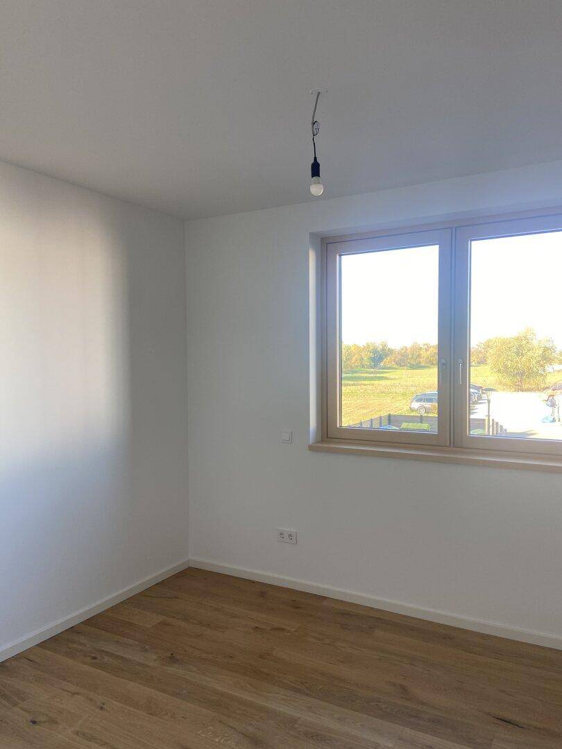 Helles Zimmer mit Holzboden und Fenster, das einen weiten Blick ins Grüne bietet.