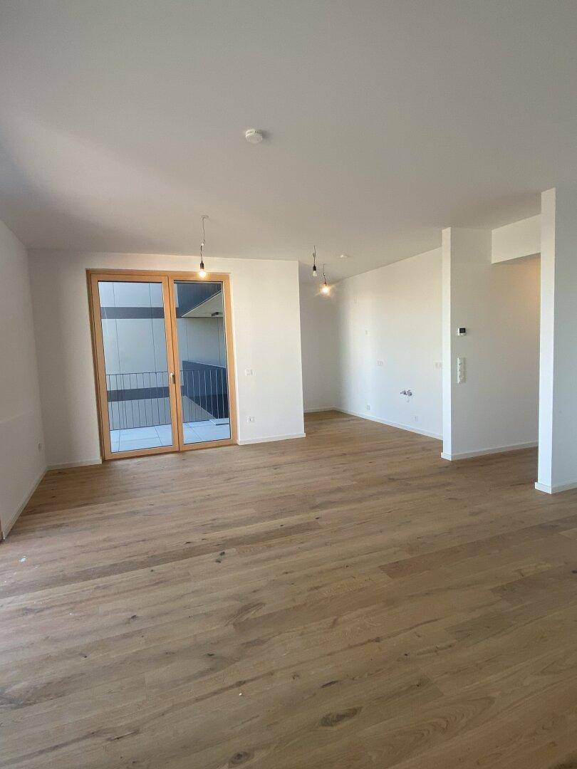 Heller Wohnbereich mit Holzboden und Zugang zu einem Außenbereich durch eine Glastür.