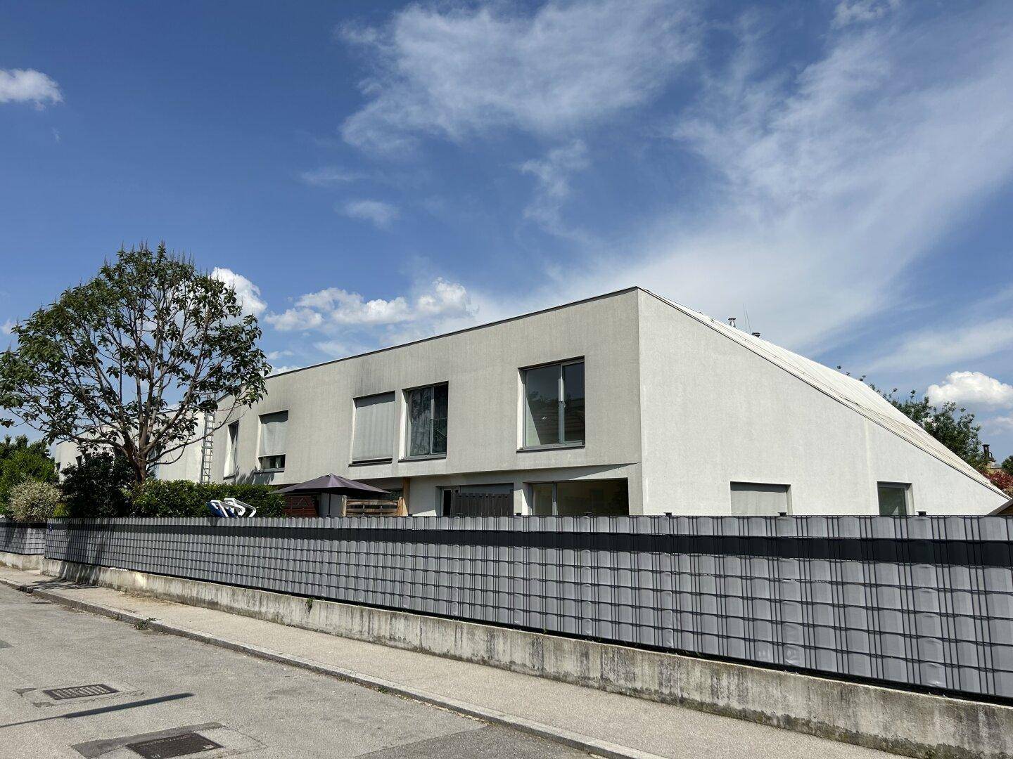 Moderne Architektur mit schräger Dachlinie und großen Fenstern, umgeben von einem Zaun.