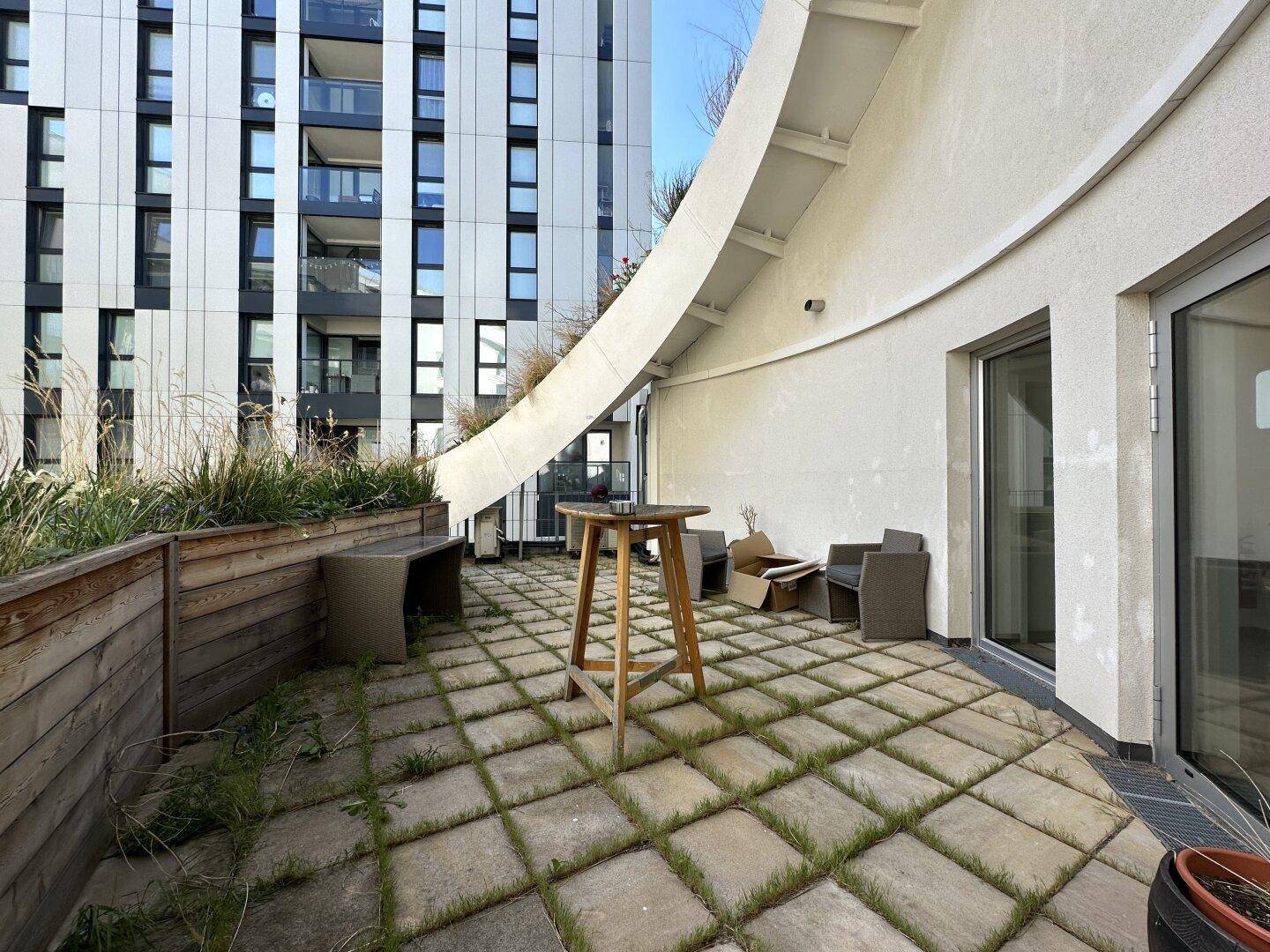 Geräumige Terrasse mit Steinplatten, Pflanzbeeten und Blick auf moderne Gebäude.