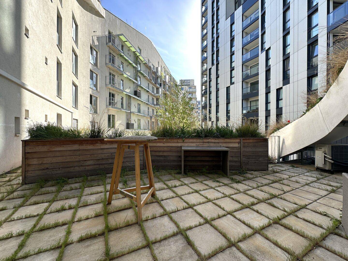Große Terrasse mit Steinplatten, Holzbeeten und Blick auf die umliegenden Gebäude.