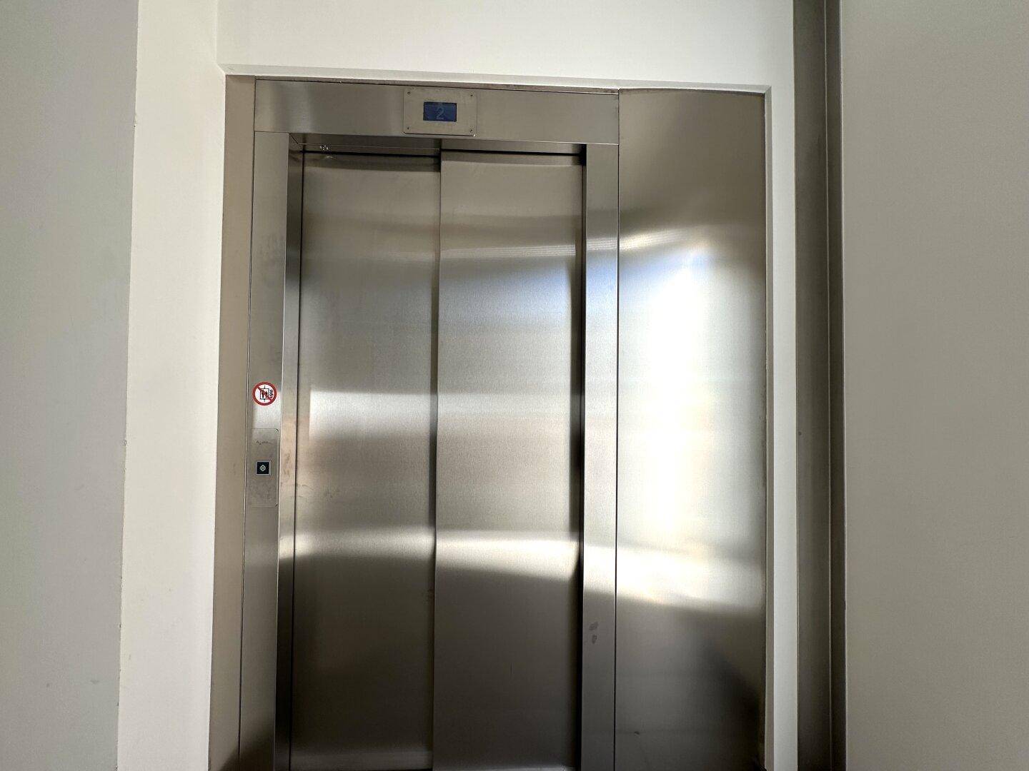Moderner Aufzug mit Edelstahltüren in einem hellen Flur.