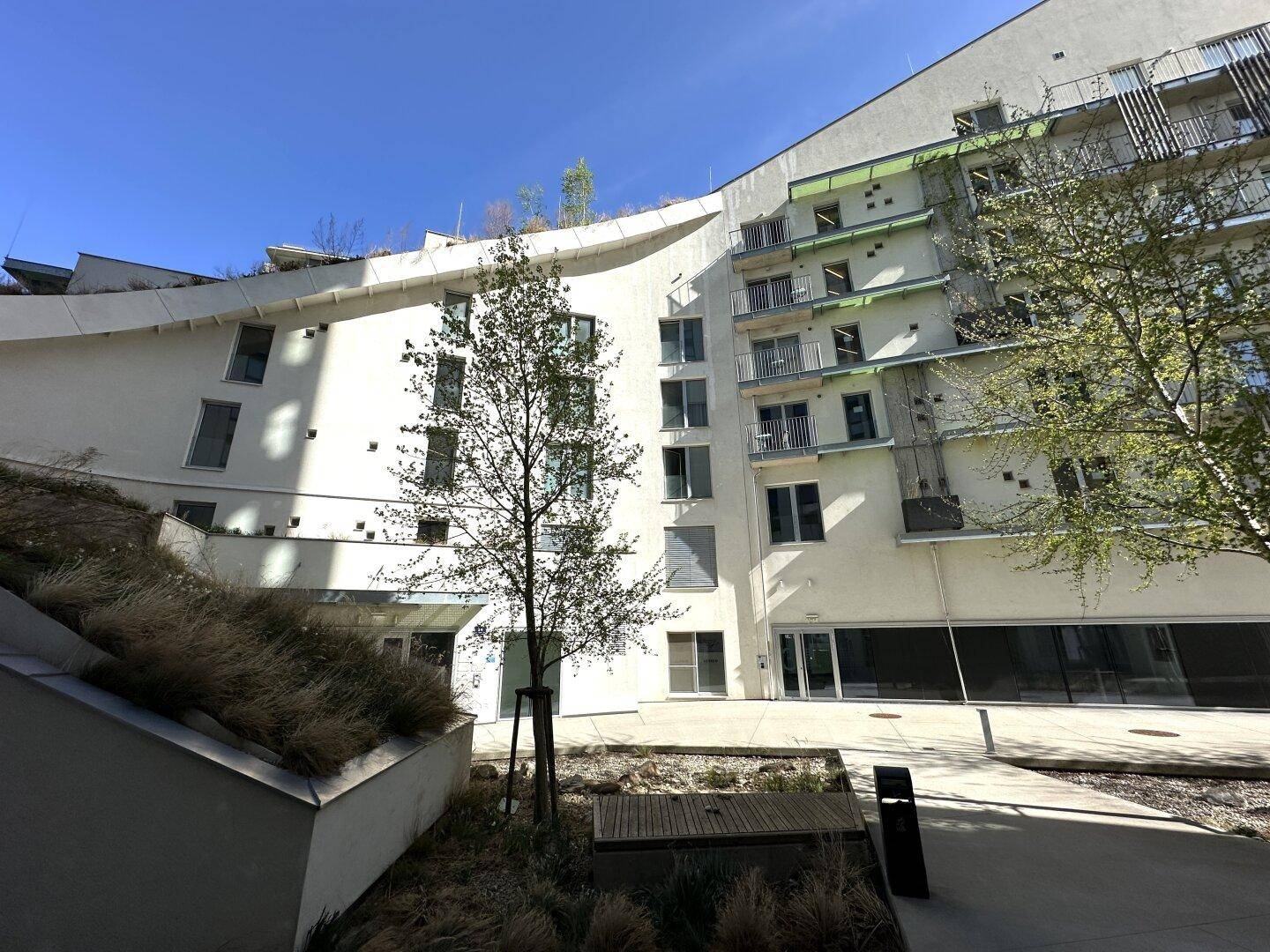 Moderne Wohnanlage mit geschwungenen Fassaden, begrünten Dächern und Bäumen.