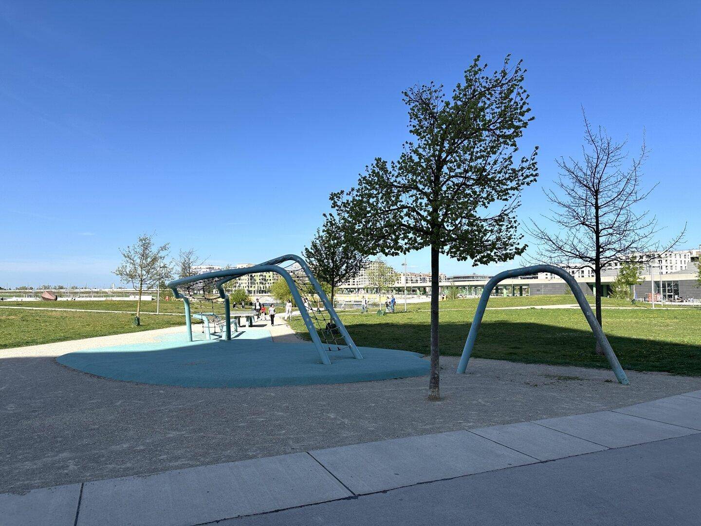 Moderner Spielplatz mit Klettergeräten und Bäumen in einer weitläufigen Grünanlage.