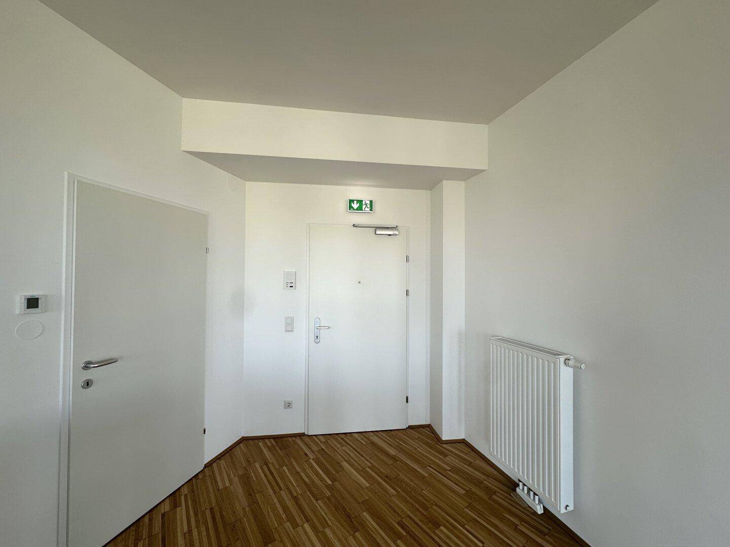 Heller Eingangsbereich mit Holzboden, weißer Heizung und zwei Türen.