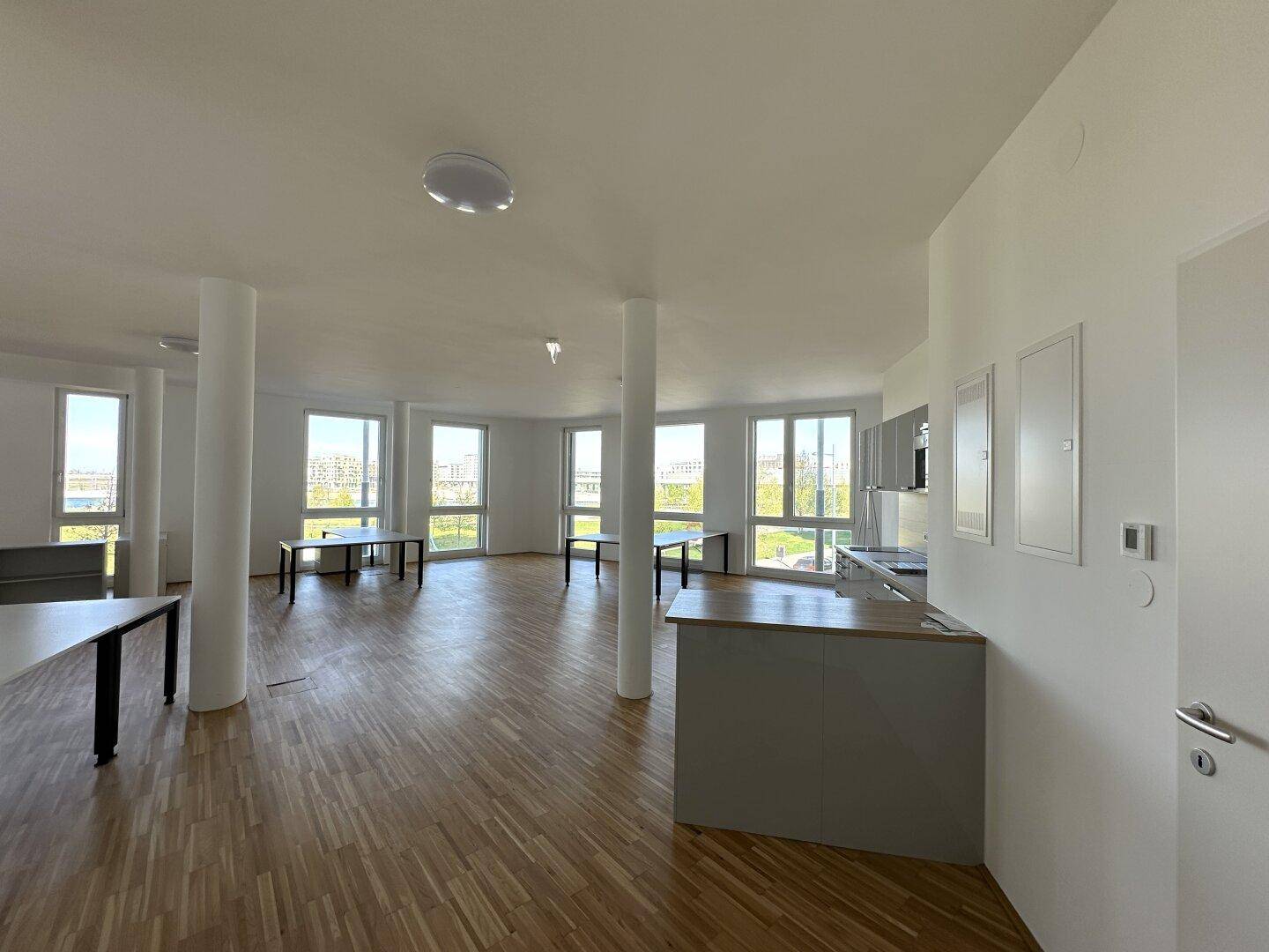Offener Bürobereich mit Küchenzeile, Holzboden und vielen Fenstern für viel Licht.