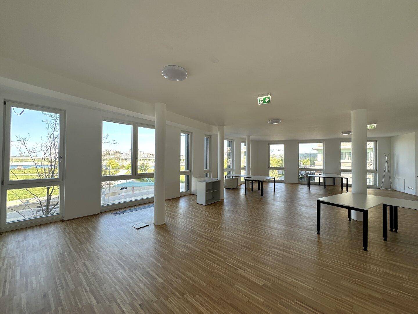 Großzügiger Büroraum mit Panoramablick durch zahlreiche Fenster und Holzboden.