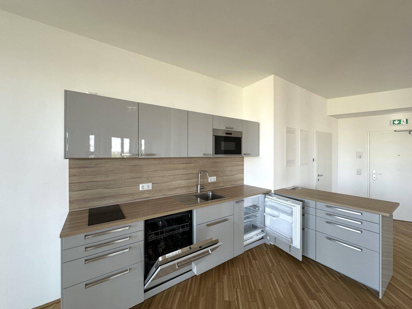 Moderne Küchenzeile mit grauen Fronten, Holzarbeitsplatte, Geschirrspüler und Kühlschrank.