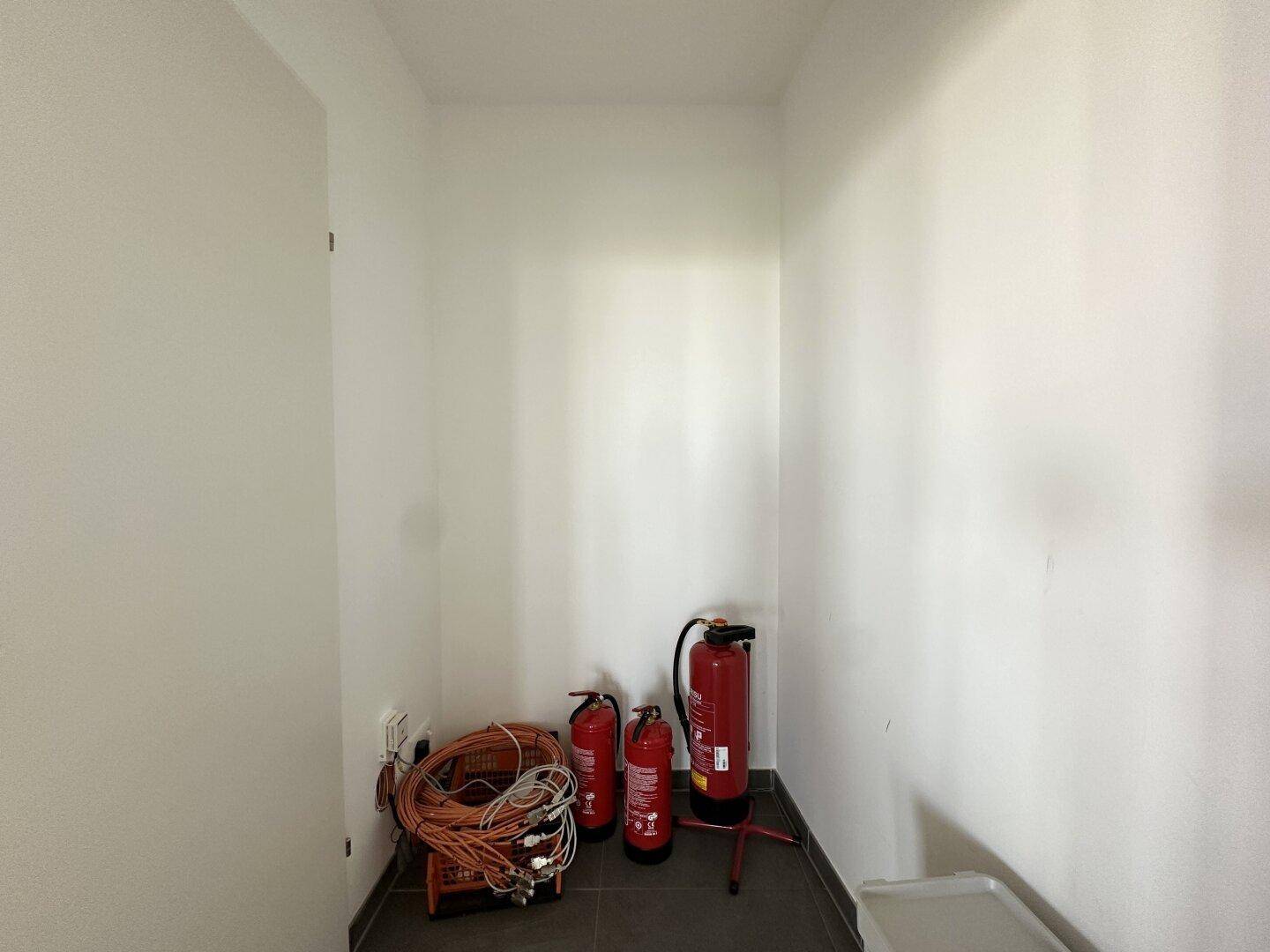 Kleiner Abstellraum mit Feuerlöschern und Kabelrollen auf dunklem Fliesenboden.