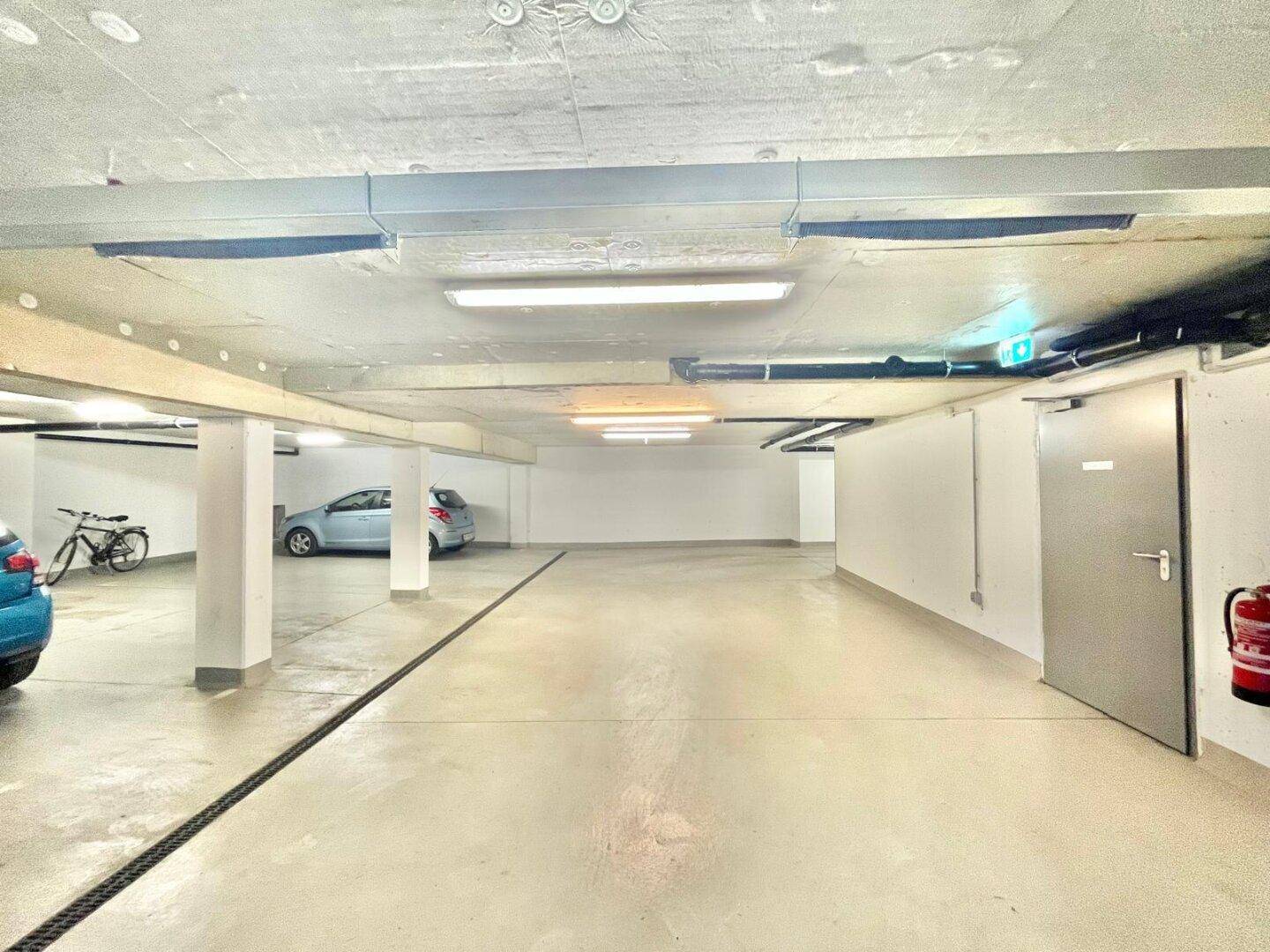 Geräumige Tiefgarage mit mehreren Stellplätzen, Autos und einem Fahrrad.
