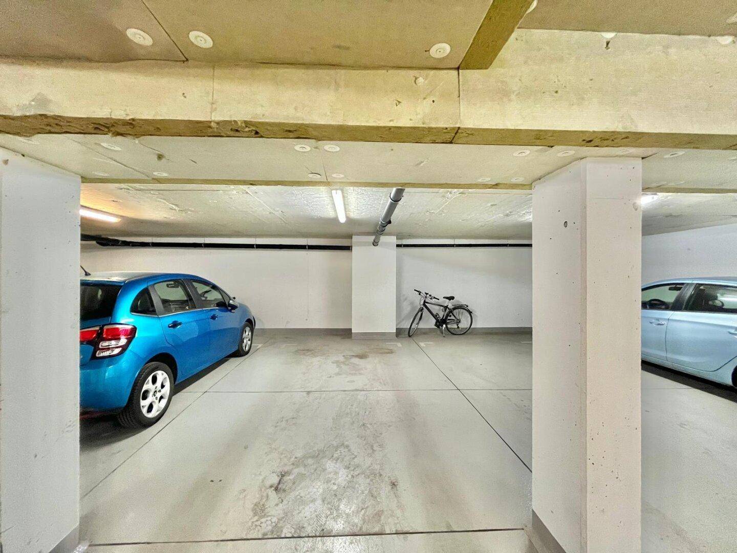 Tiefgaragenbereich mit einem geparkten blauen Auto, einem Fahrrad und Betonsäulen.