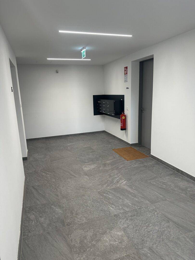 Heller Eingangsbereich mit modernen Fliesen, Briefkästen und einem Feuerlöscher an der Wand.