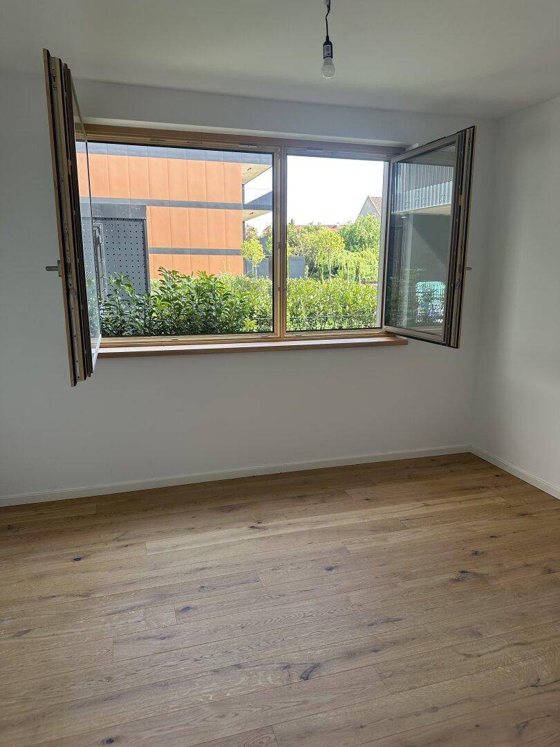 Helles Schlafzimmer mit Eichenparkettboden und einem großen Fenster mit Blick ins Grüne.