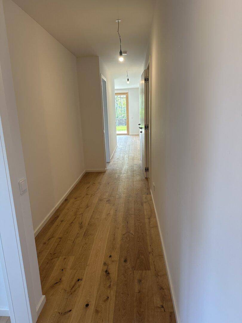 Langer, heller Flur mit hochwertigem Eichenparkettboden und weißen Wänden.
