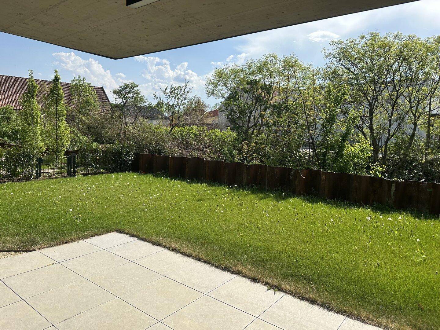 Private Gartenfläche mit Rasen und einer gepflasterten Terrasse, umgeben von Hecken und Bäumen.