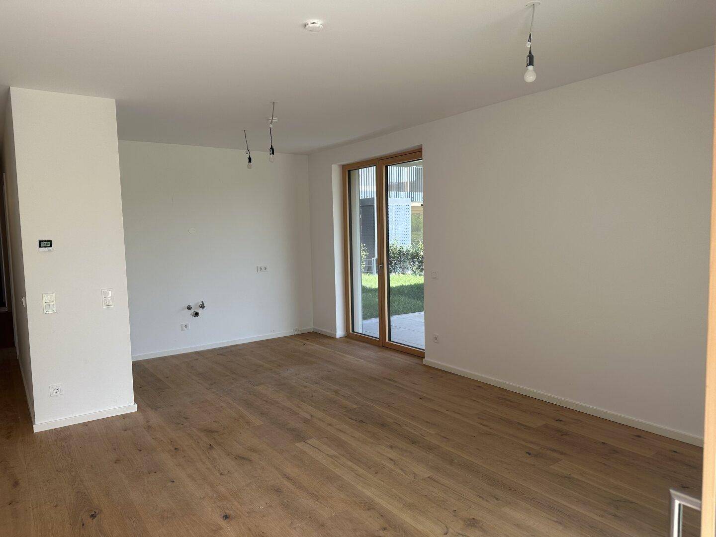 Heller, leerer Raum mit Eichenparkettboden und großer Terrassentür, die viel Tageslicht hereinlässt.