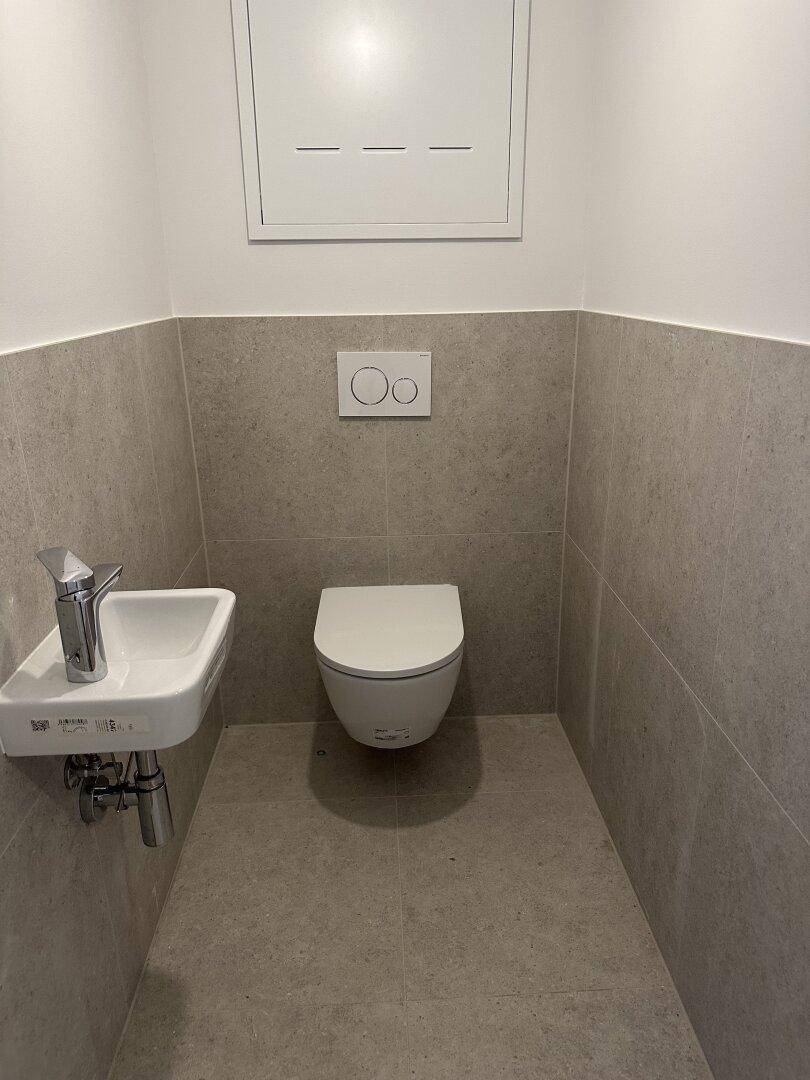 Modernes Gäste-WC mit wandhängender Toilette und kleinem Waschbecken in neutralen Farben.