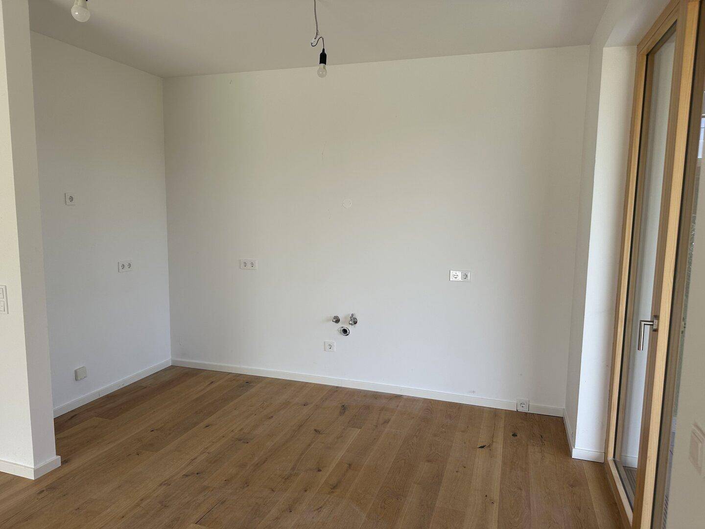 Heller, unmöblierter Wohnraum mit Eichenparkettboden und Zugang zu einem Außenbereich.