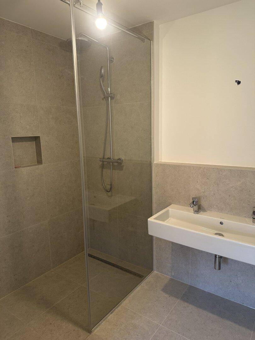 Modernes Badezimmer mit ebenerdiger Dusche, Doppelwaschbecken und großformatigen Fliesen.