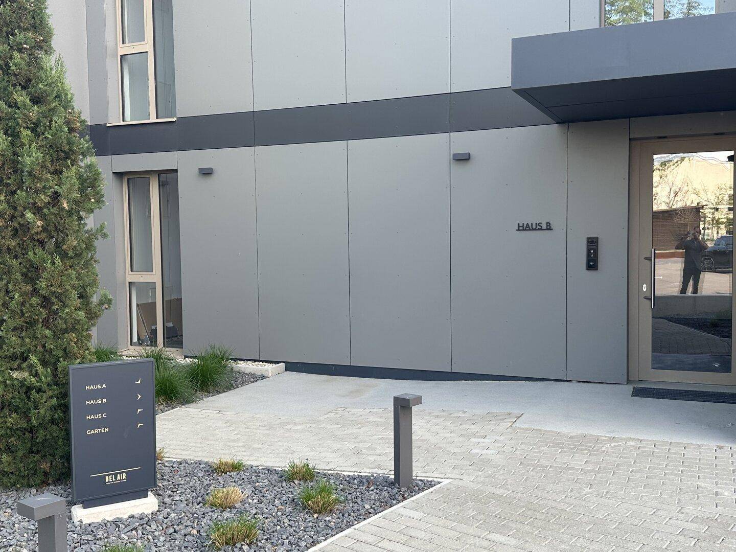 Eingangsbereich von Haus B mit moderner Beschilderung und gepflegter Außenanlage.