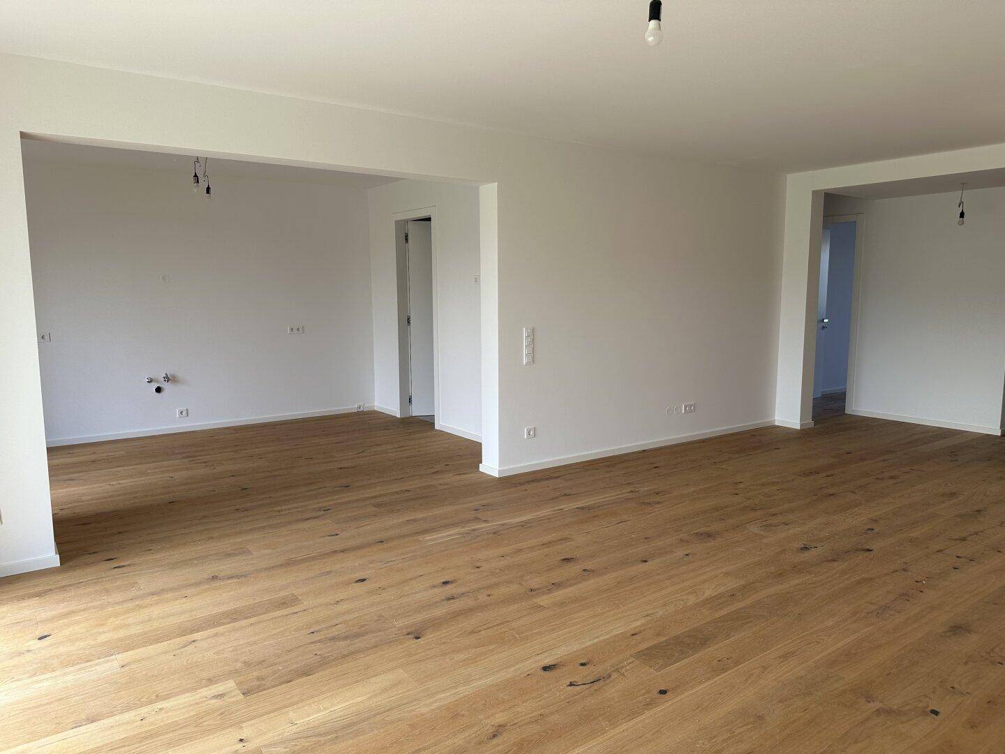 Geräumiger, offener Wohnbereich mit hellem Holzboden und mehreren Türöffnungen.