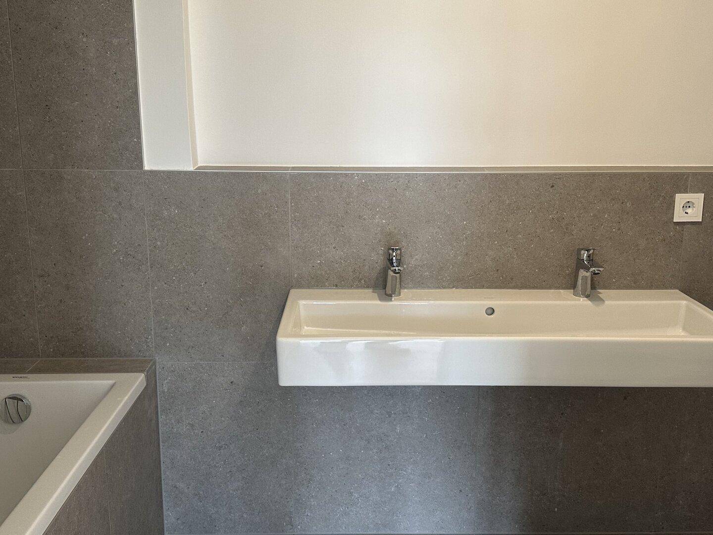 Modernes Badezimmer mit Doppelwaschbecken, Badewanne und grauen Wandfliesen.