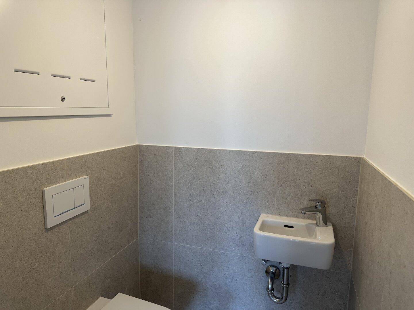 Modernes Gäste-WC mit kleinen Waschbecken und grauen Fliesen an den Wänden.