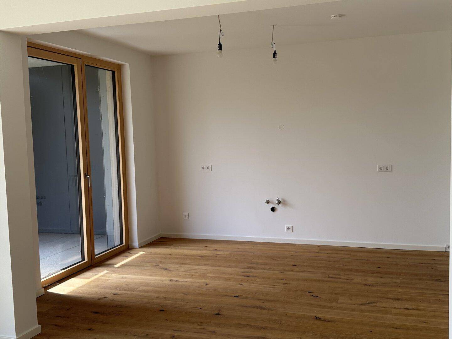 Heller, leerer Raum mit Eichenparkettboden und großem Fenster, das viel Tageslicht hereinlässt.
