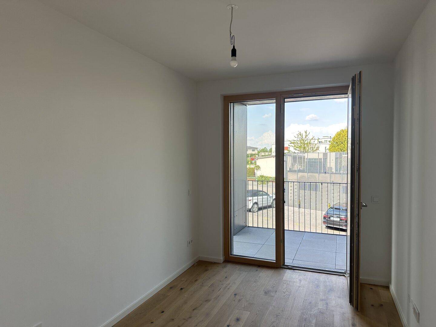 Helles, leeres Zimmer mit Eichenparkettboden und direktem Zugang zu einem kleinen Balkon.