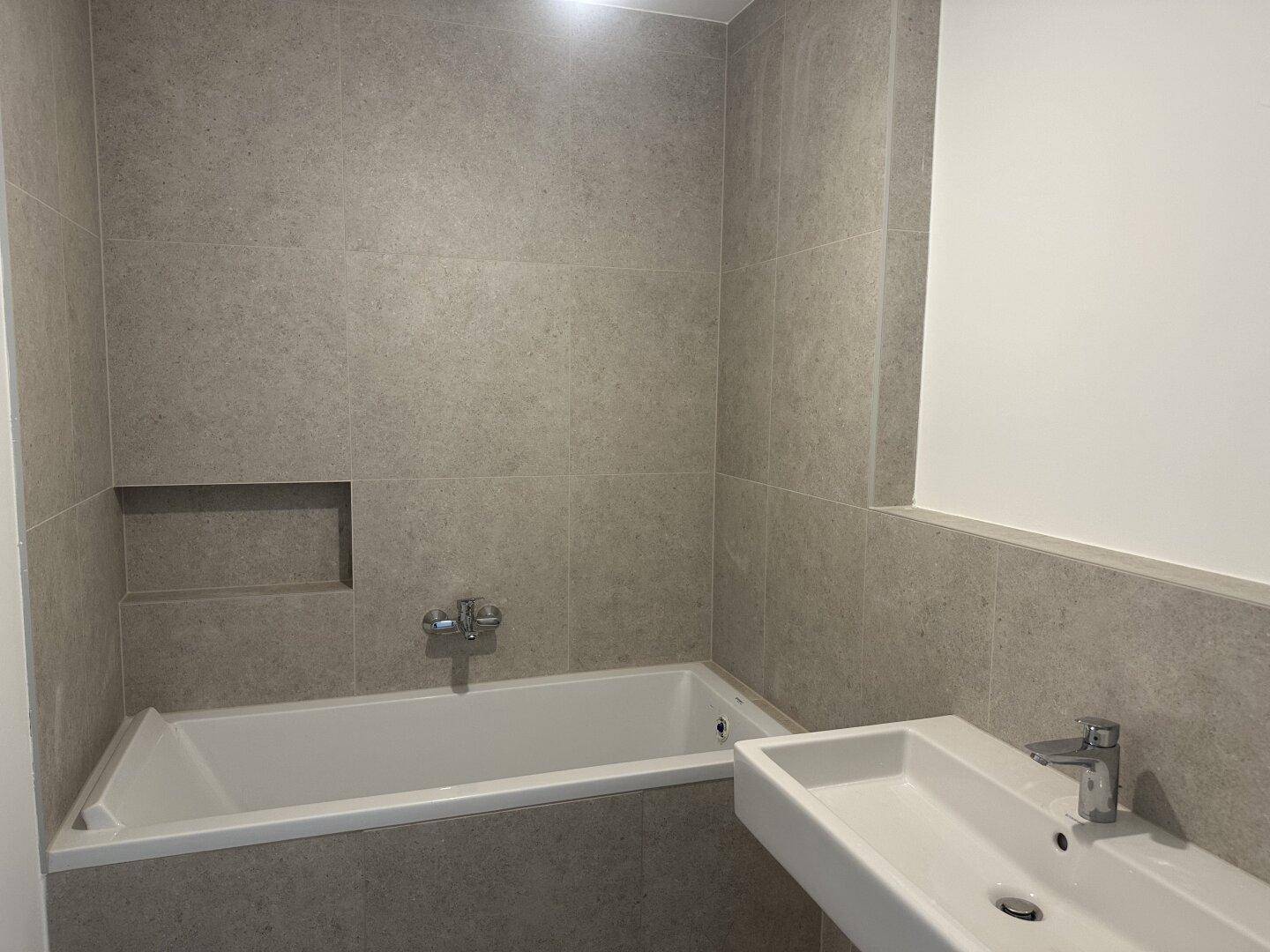 Modernes Badezimmer mit Badewanne, integrierter Nische und elegantem Waschbecken.