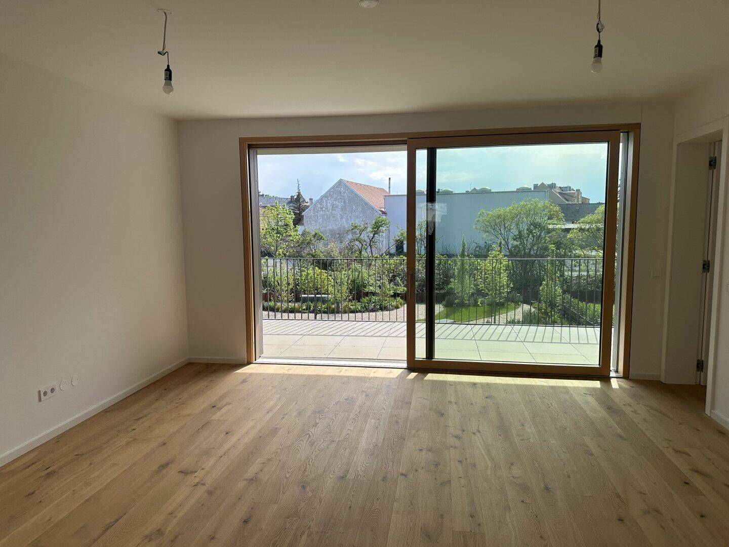 Helles, leeres Wohnzimmer mit Eichenparkettboden und großzügigem Zugang zu einem Balkon.
