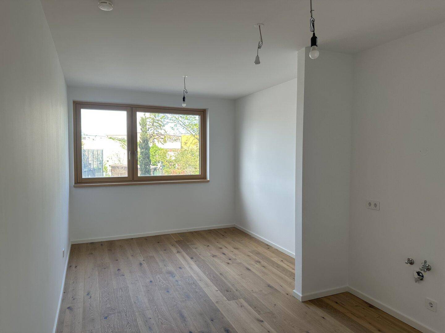 Leeres Zimmer mit hellem Eichenparkettboden und einem Fenster, ideal als Schlaf- oder Arbeitszimmer.