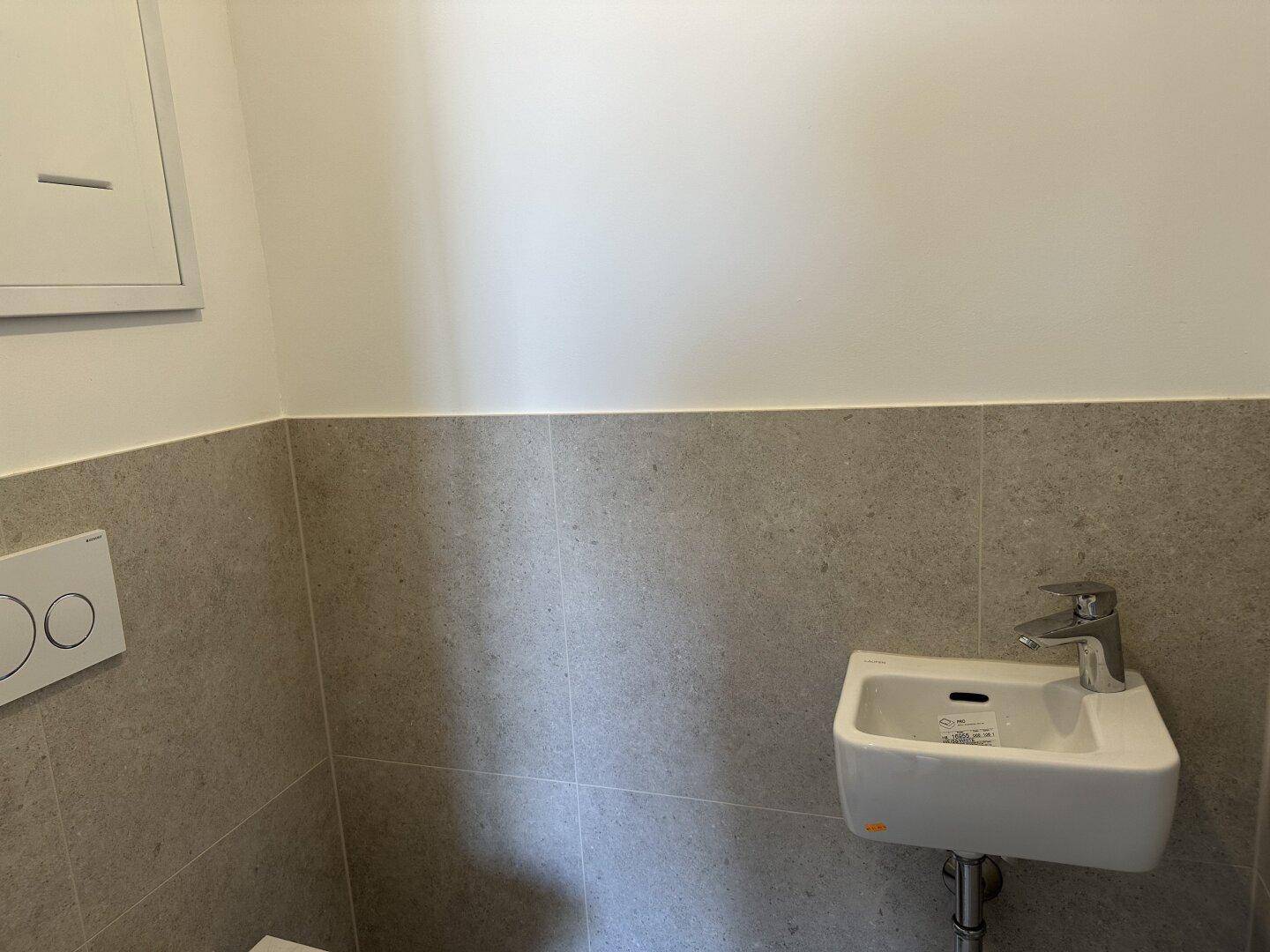 Modernes Gäste-WC mit grauen Fliesen, wandhängendem WC und kleinem Waschbecken.