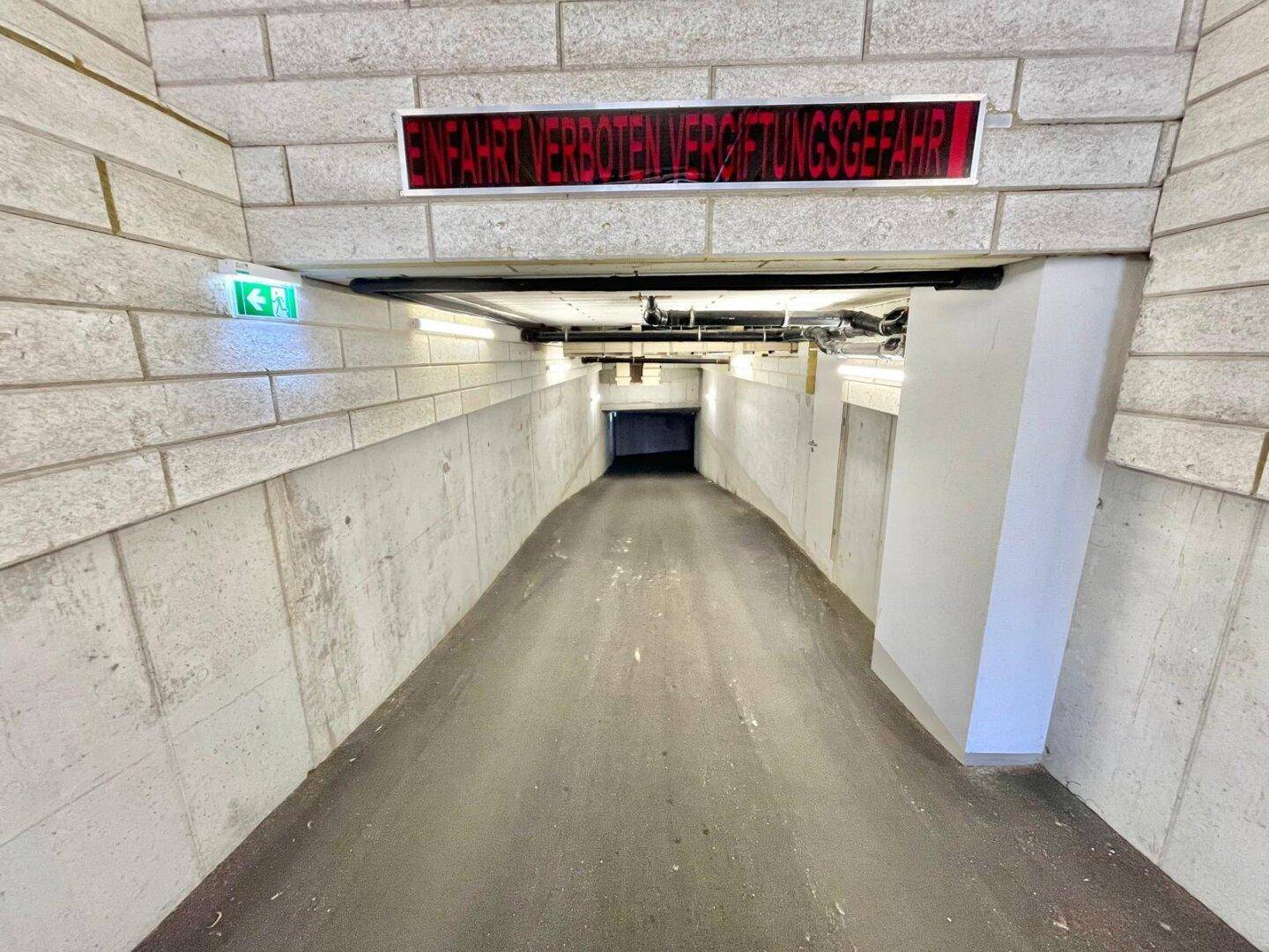 Einfahrt zu einer Tiefgarage mit Warnschild und Betonwänden, die in den Untergrund führt.