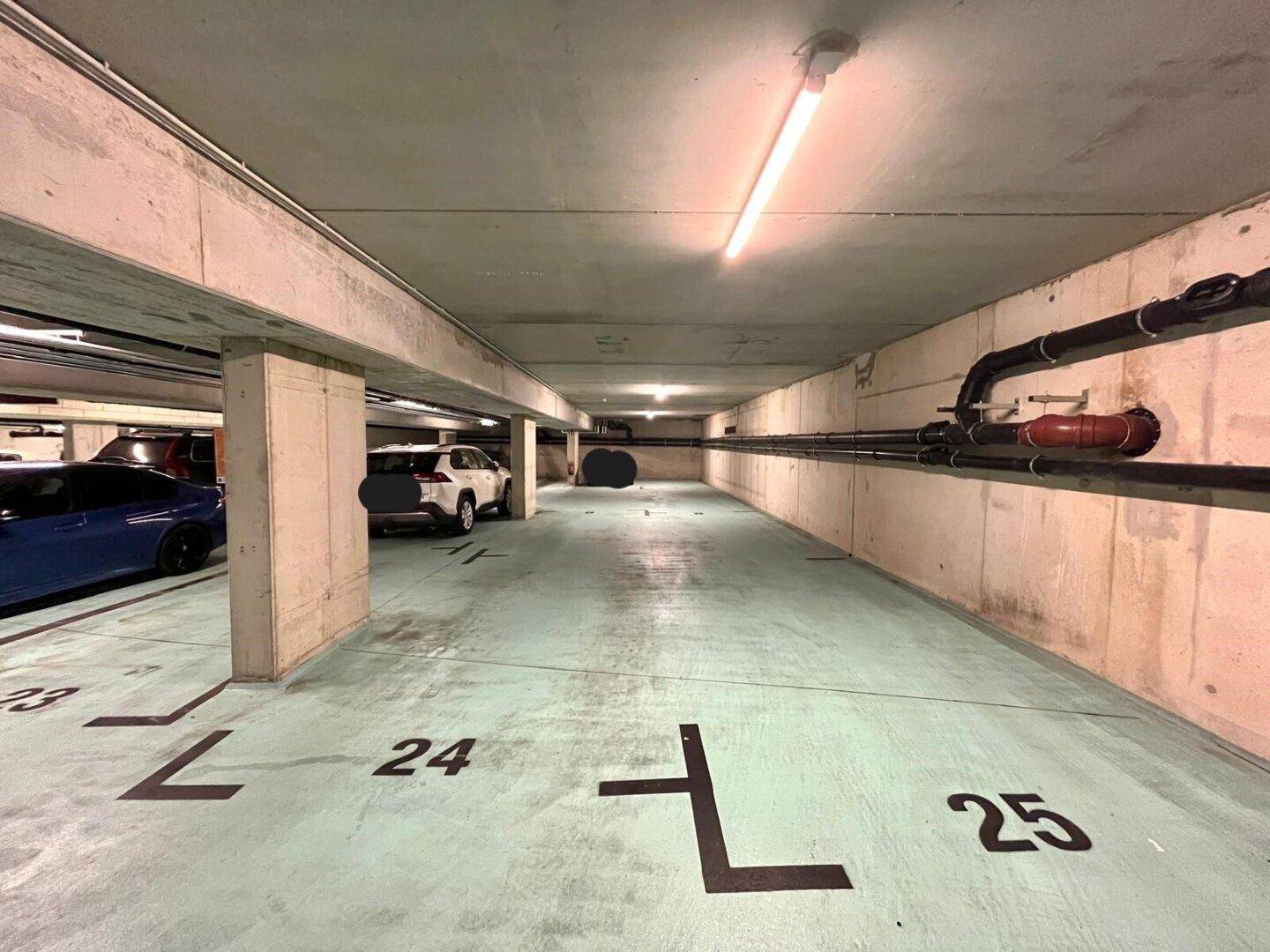 Weitere Ansicht der Tiefgarage mit nummerierten Stellplätzen und sichtbaren Rohrleitungen an der Decke.