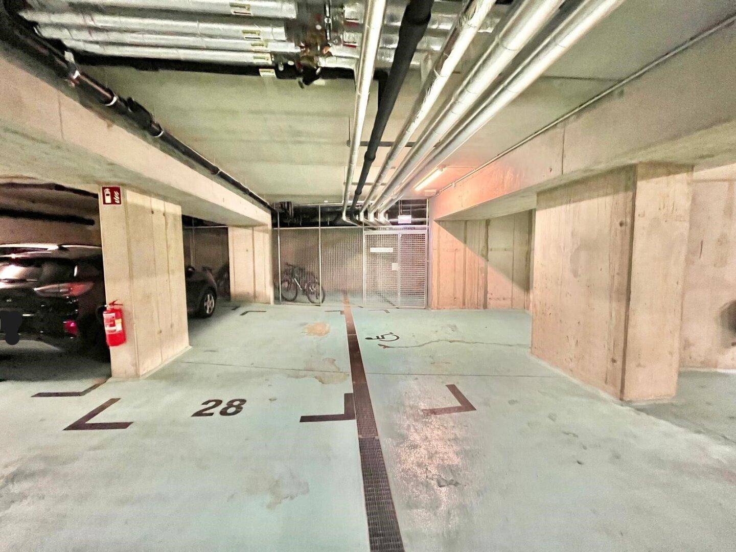 Bereich der Tiefgarage mit weiteren Stellplätzen, einem Fahrrad und einem Feuerlöscher an der Wand.