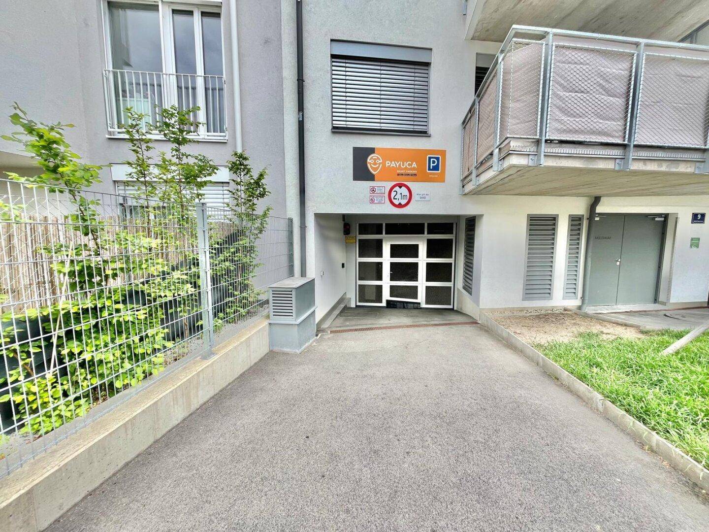 Äußerer Eingangsbereich einer Tiefgarage mit Zufahrt, Beschilderung und Höhenbegrenzung am Gebäude.
