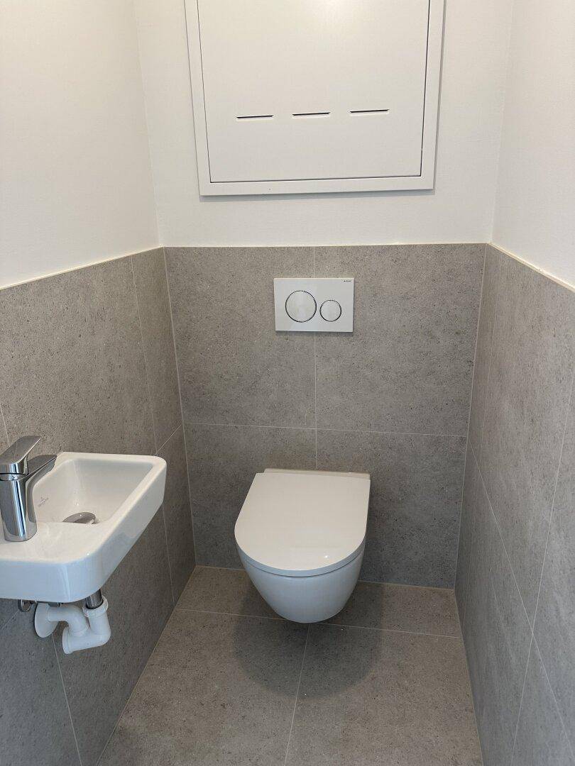 Modernes Gäste-WC mit wandhängender Toilette und kleinem Waschbecken.