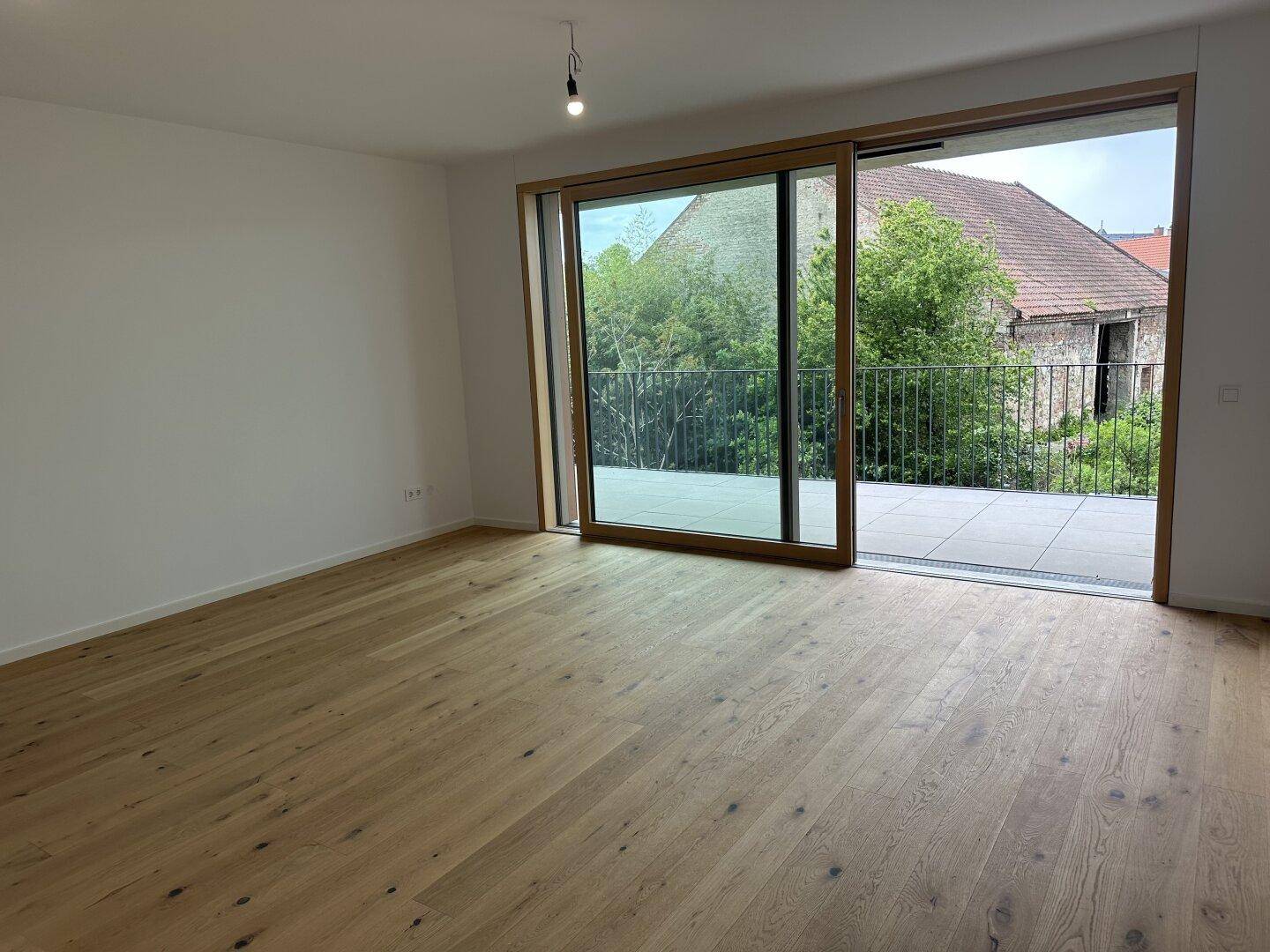 Heller Raum mit Eichenparkett und großer Schiebetür, die auf einen Balkon führt.