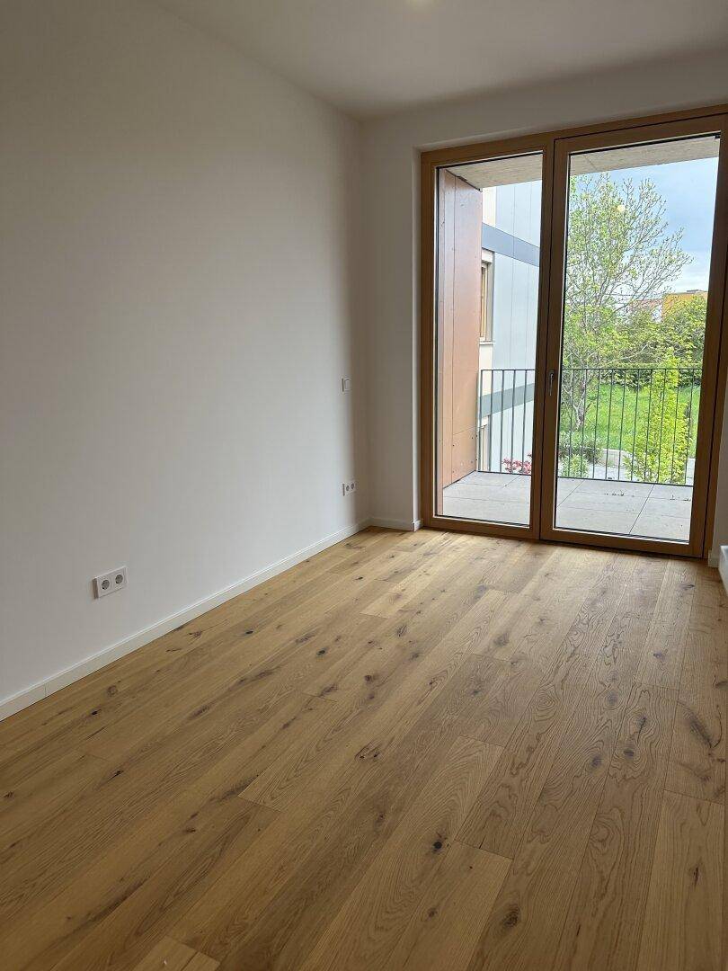 Helles Schlafzimmer mit Eichenparkettboden und Zugang zu einem Außenbereich.