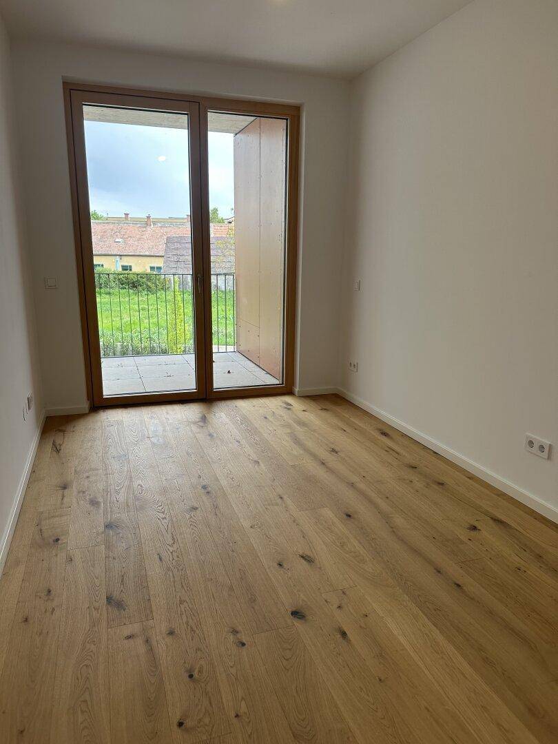 Geräumiges Schlafzimmer mit Holzboden und großen Fenstern, die viel Licht hereinlassen.