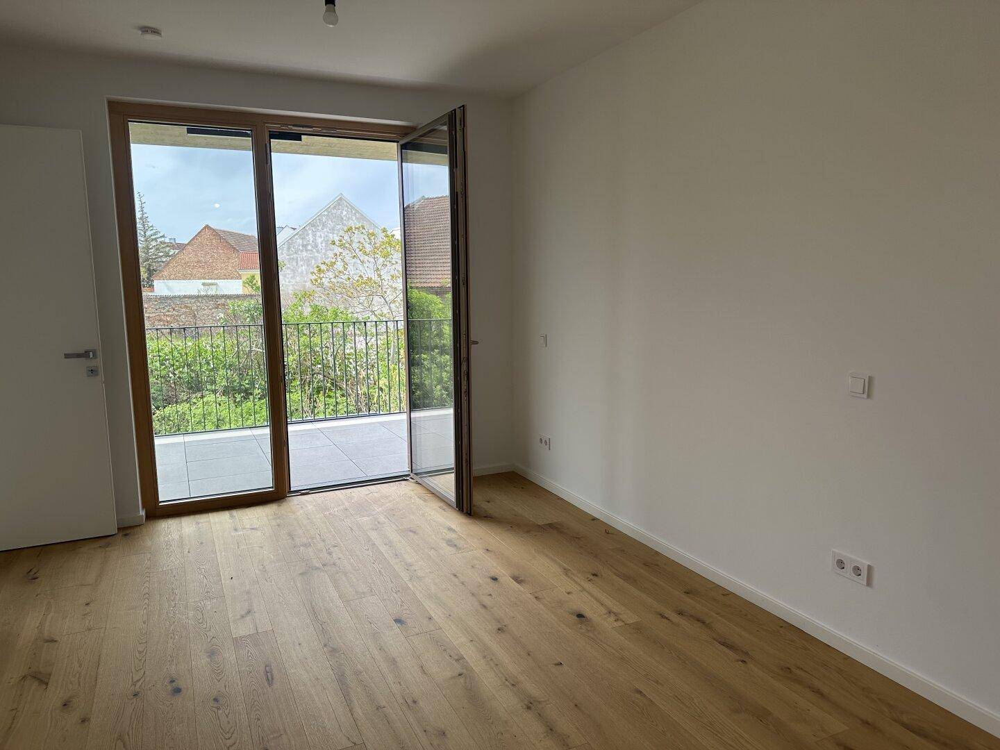 Heller Wohnraum mit Eichenparkettboden und direktem Zugang zu einem Balkon oder einer Terrasse.