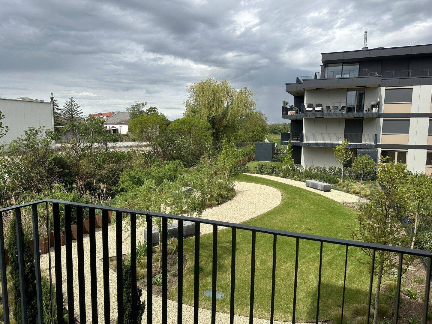 Blick vom Balkon auf eine gepflegte Gartenanlage und weitere moderne Gebäude.