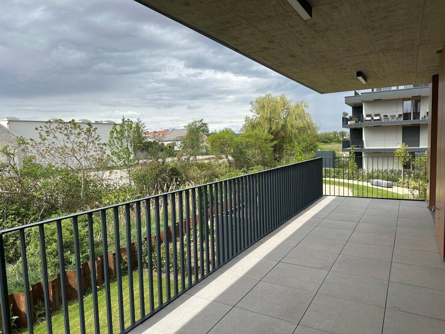 Großer Balkon mit Fliesenboden und Blick auf die grüne Umgebung und weitere Gebäude.