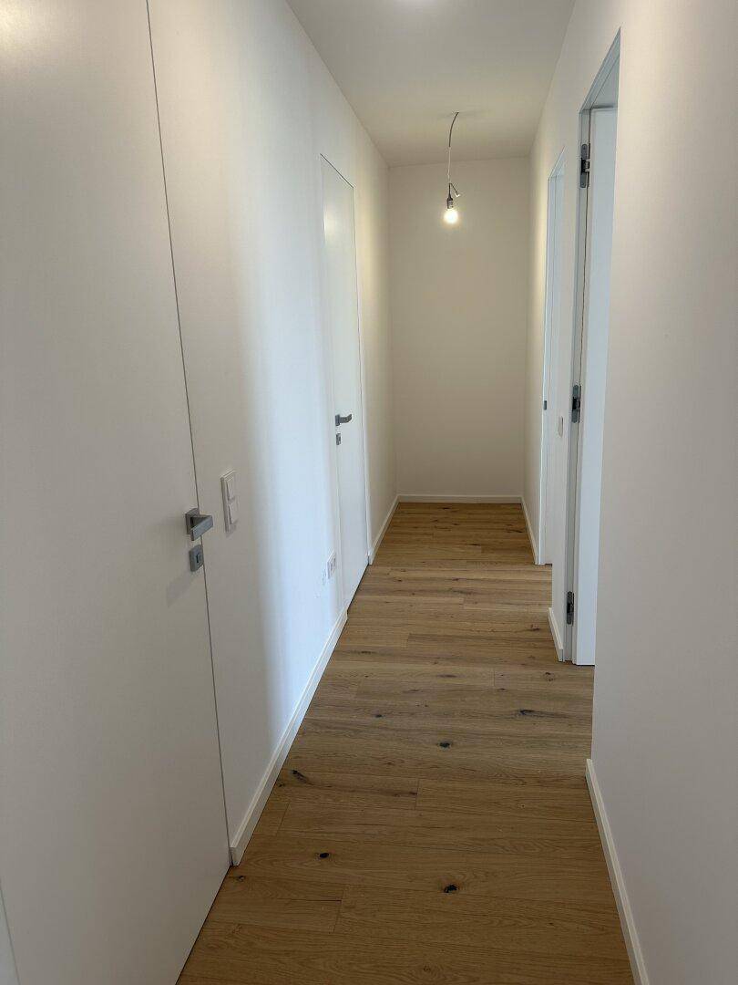 Heller Flur mit Eichenparkettboden und weißen Wänden, der zu weiteren Räumen führt.