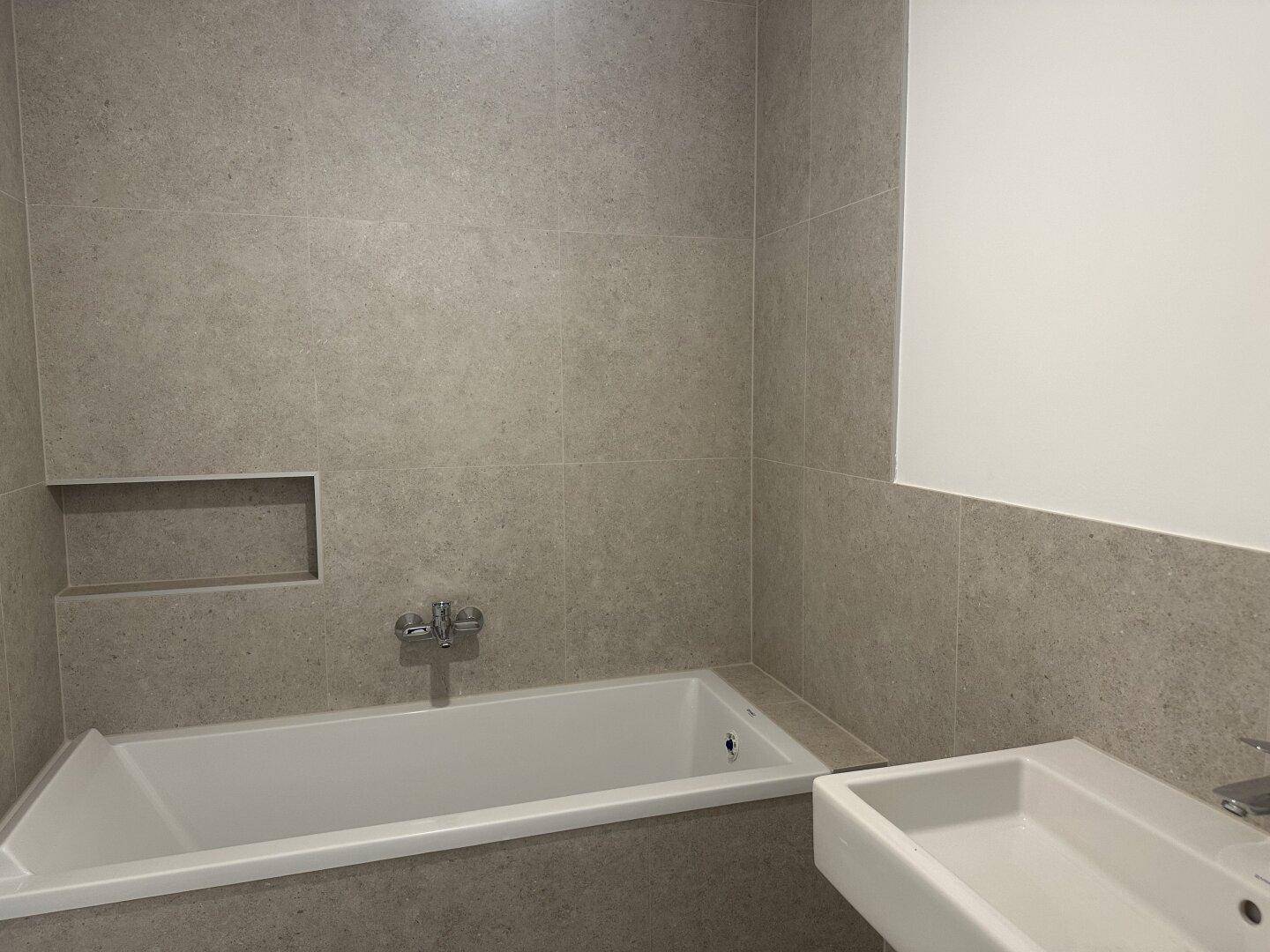 Modernes Badezimmer mit Badewanne, Waschbecken und hellgrauen Wandfliesen.