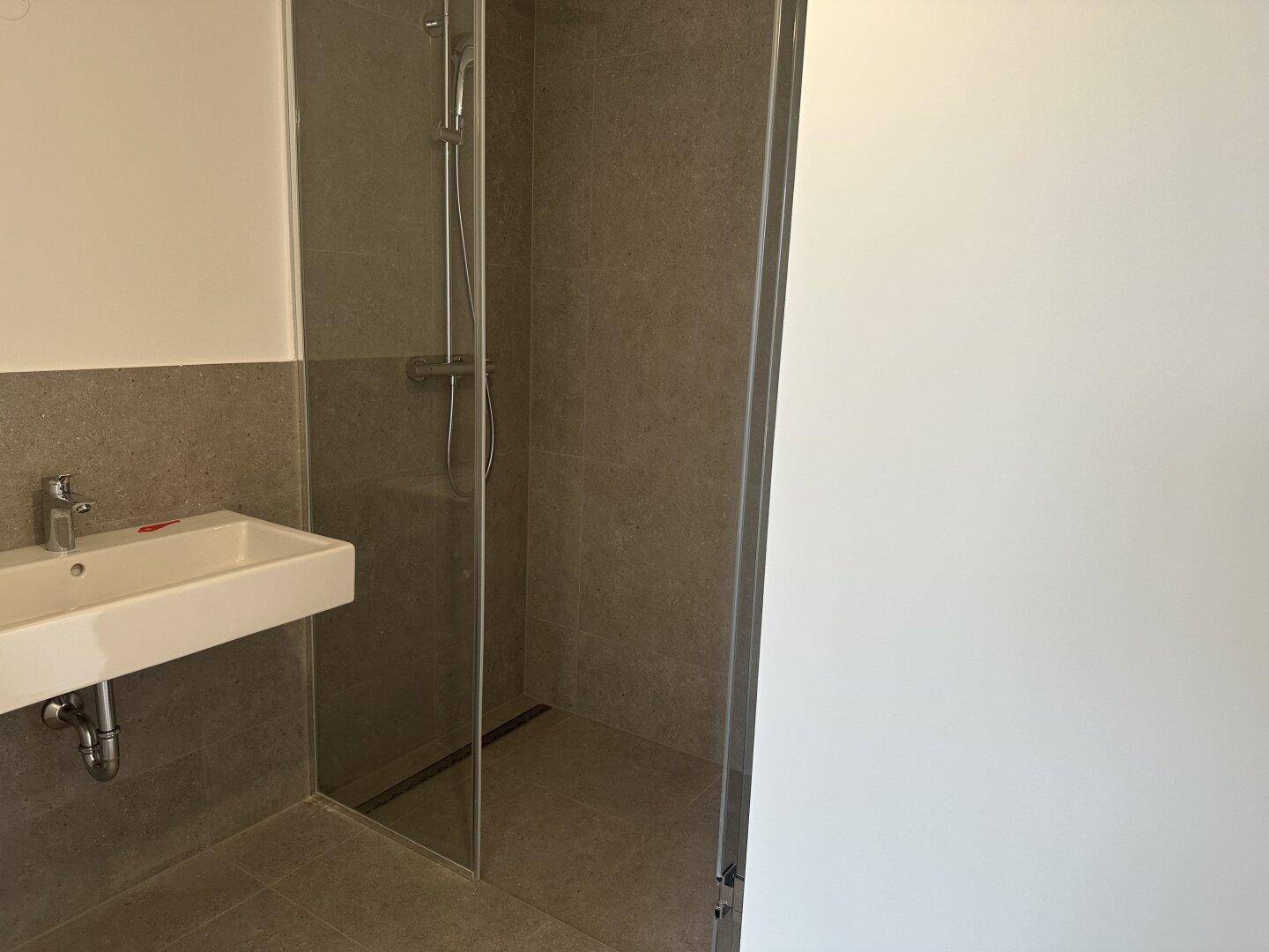 Modernes Badezimmer mit ebenerdiger Dusche und hellgrauen Fliesen.